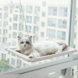 White cat resting on a hanging cat window hammock attached to a glass window with suction cups for birdwatching and sunbathing.