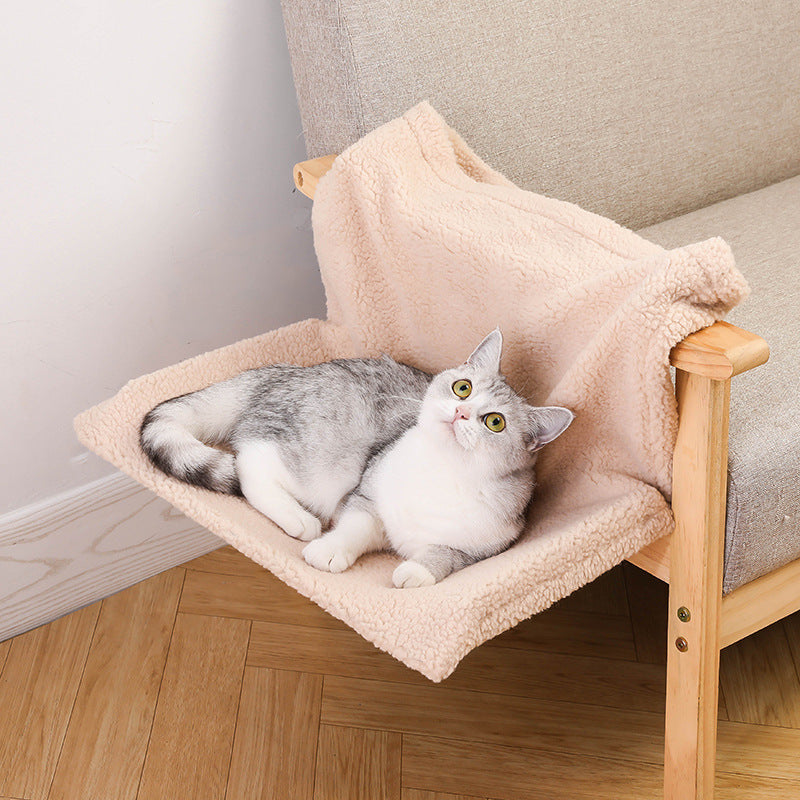 Plush L-shaped cat hammock in beige hanging on wooden armchair with gray and white cat lounging