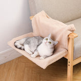 Plush L-shaped cat hammock in beige hanging on wooden armchair with gray and white cat lounging