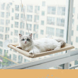 White cat lounging on a beige hanging cat window hammock by a city window