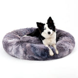 Black and white dog resting on a gray fluffy donut dog bed designed for calming and comfort for cats and dogs