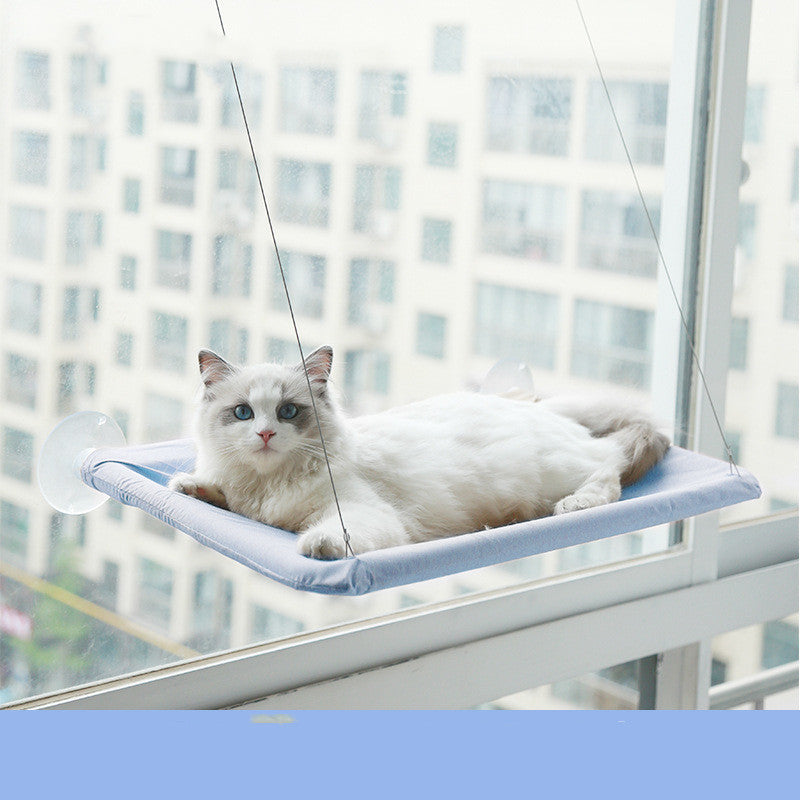 White cat resting on a blue hanging cat window hammock attached with suction cups on a window.