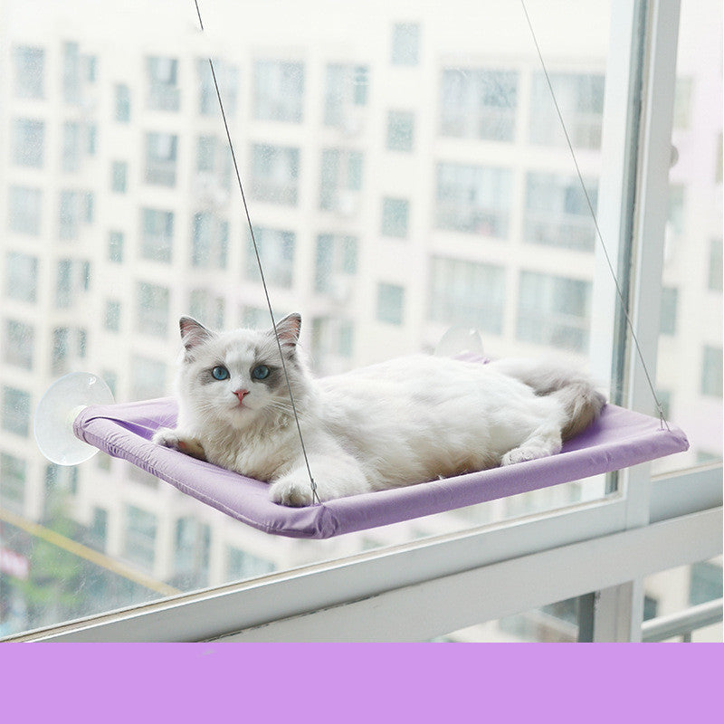 White cat lounging on a purple hanging cat window hammock designed for birdwatching and sunbathing.