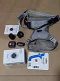 Pet Tracker Collar Camera set with gray adjustable strap harness, remote control, camera lens, protective shell, charging cable, 32GB memory card, and user manual on brown background